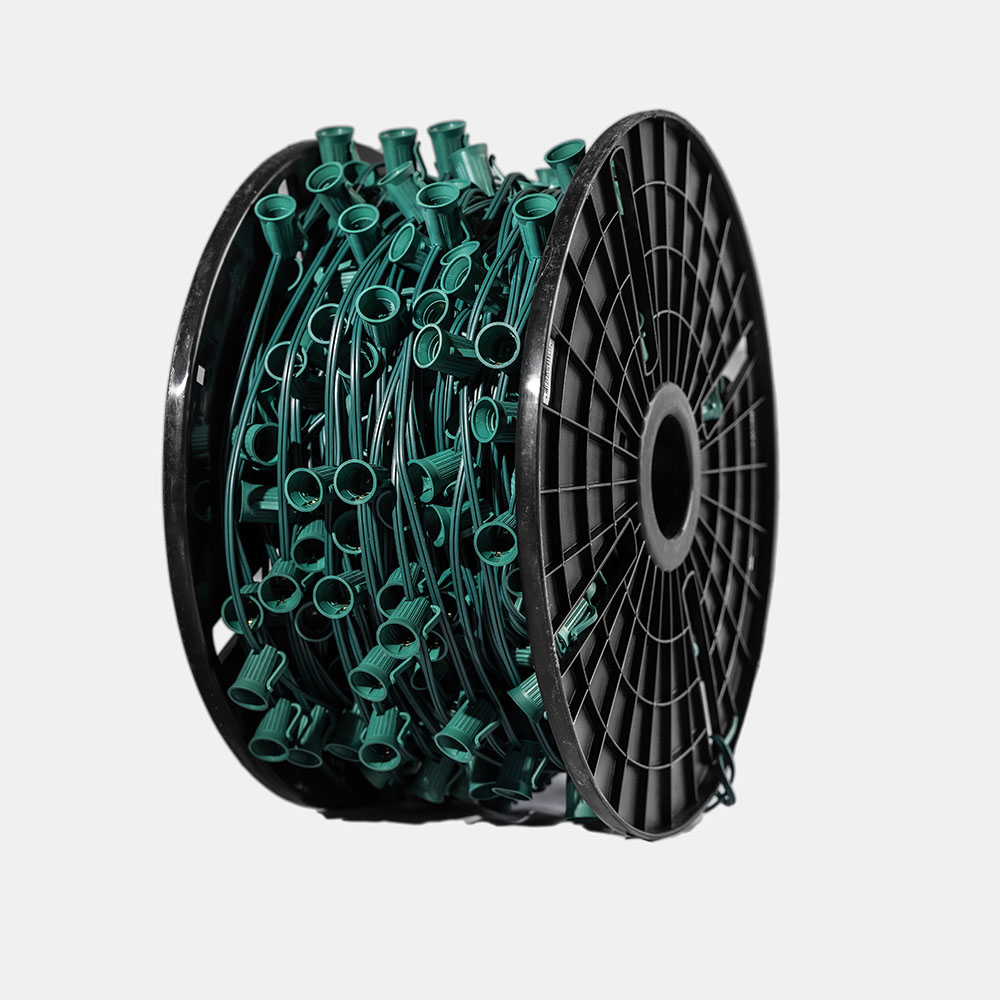 A large plastic spool fully wrapped with a long string of green outdoor lighting wire and empty light bulb sockets.