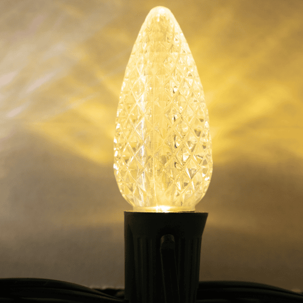 Close-up of a lit C9 LED Christmas bulb in Sun Warm White (deep amber/yellow color) with a faceted, diamond-cut lens. C9 Sun Warm White Faceted HBL